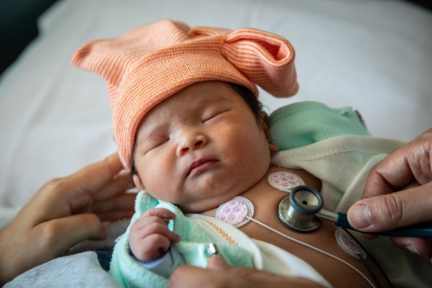A baby in the NICU, with stethoscope listening to her lungs.